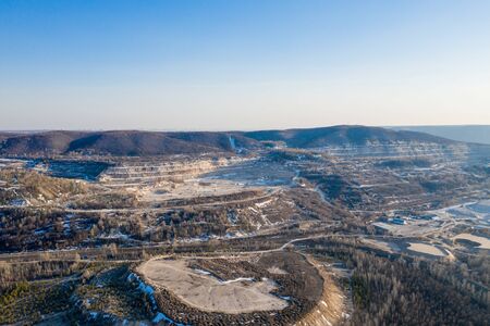Old stone quarry opencast mine on river side in forest at winter