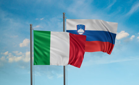 Slovenia and Italy flag waving together in the wind on blue sky, two country cooperation conceptの写真素材