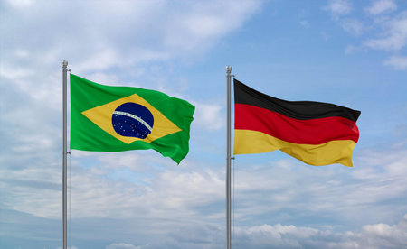 Germany and Brazil flags waving together on blue cloudy sky, two country relationship conceptの写真素材