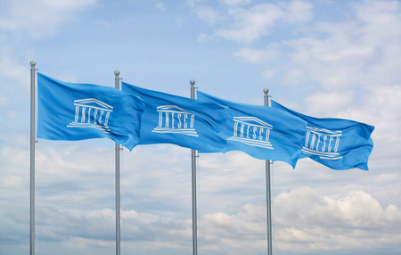 UNESCO four flags in row waving together on blue cloudy sky, cooperation concept