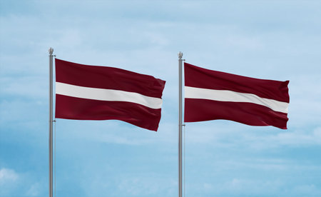 Two Latvia flags waving together in the wind on blue cloudy sky, two country relationship conceptの写真素材
