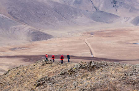 Tourists wearing red and blue clothes having rest on the top of mountain. Mountain valley landscape.の写真素材