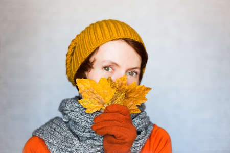 Beautiful happy woman wearing knitted clothes holds autumn yellow leaves near the face.の写真素材