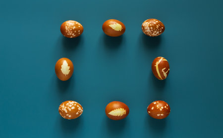 Eggs decorated with organic onion paint and leaves of plants on Easter holiday. Blue background.の写真素材