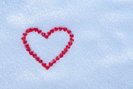 Red heart made with lots of little hearts on snow surface.