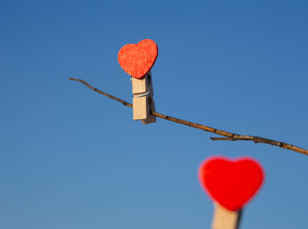 Wooden clothespins with red hearts on tree branches on blue sky backgroud. Selective blurred focus. Wedding, date or Valentines day concept.の写真素材
