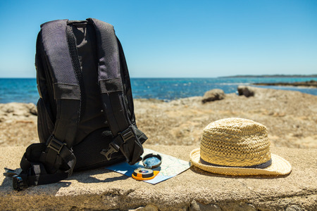 Travel concept with backpack, map, compass and straw hat on a seashore backgroundの写真素材