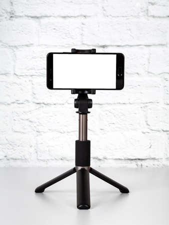 Mockup with smartphone on a tripod with empty screen on office table and brick wall background. Cope spaceの写真素材