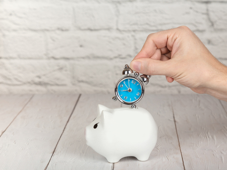 Saving time concept. Hand putting alarm clock into the piggy bank. Copy space