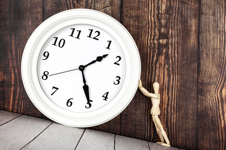 Wooden human figure holding the clock on the inclined table. Control of time or time management...