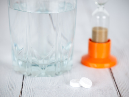 Time to take the medicine. Pills, glass of water and hourglass on wooden table