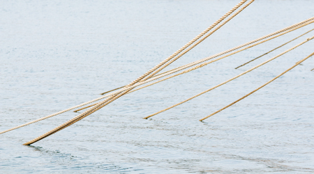 Stretched mooring ropes going out from the sea water  surfaceの写真素材