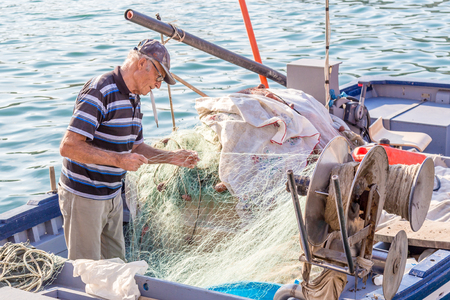 20 October 2014. Syracuse, Italy: Senior fisherman unraveling the net on the boatの写真素材