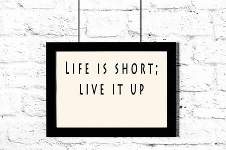 Black frame with wise quote hanging on a white brick wall.の写真素材