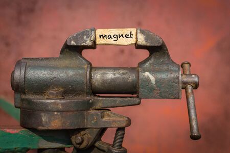 Concept of dealing with problem. Vice grip tool squeezing a plank with the word magnetの写真素材