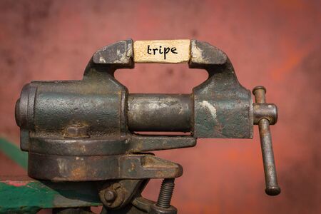 Concept of dealing with problem. Vice grip tool squeezing a plank with the word tripeの写真素材
