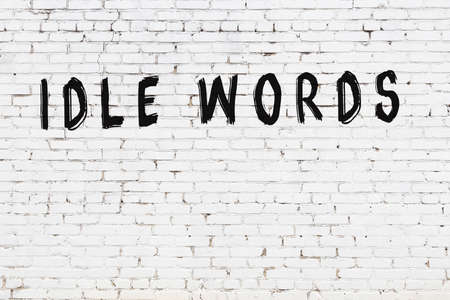 Inscription idle words written with black paint on white brick wall.の写真素材