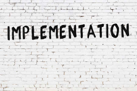 White brick wall with inscription implementation handwritten with black paintの写真素材