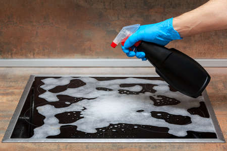 Cleaning the electric stove with household chemicals. An adult man's hand in a blue glove holds a...