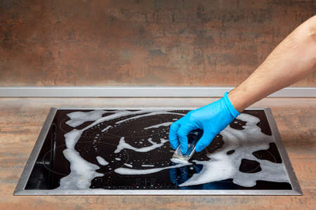 Hand in blue glove washes the modern electric stove with a scraperの写真素材