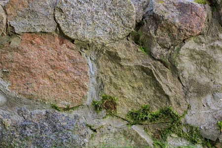 Old retaining wall of chipped granite cobblestones with moss growing from the seams. Close-up viewの写真素材