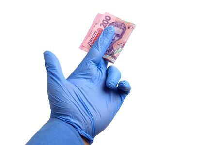 A hand in a medical glove holds Ukraine state money, hryvnia, on a white background isolated....