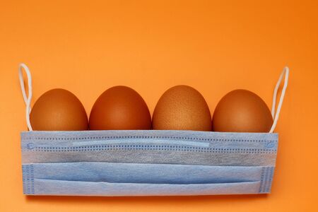 Chicken eggs and medical mask on a yellow background, metaphor with a basket. The concept of Easter...