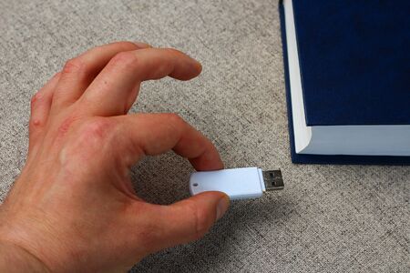 A flash drive in hand on a background of a book. Knowledge loading metaphorの写真素材