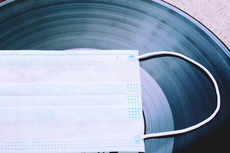 Vinyl audio record and medical surgical mask, abstract concept of nostalgia for music and concerts under quarantine and self-isolation due to the pandemic of Covid-19 (coronavirus)の写真素材
