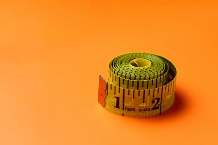 Inch and centimeter tape on a trendy in advertising orange background with copy space for an inscription or textの写真素材