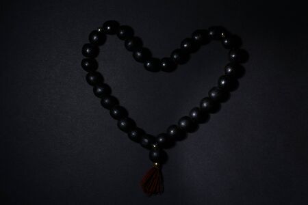 Black rosary in the shape of a heart on a black background in a dark low key