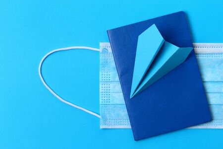 Paper airplane and passport on a blue background with a medical maskの写真素材