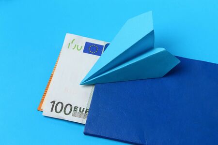 Airplane made of paper on a blue background with a passport and euro, the concept of a flight ban due to an epidemic or pandemicの写真素材