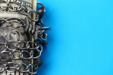 Dollar wrapped in a chain on a blue background with place for an inscription or textの写真素材