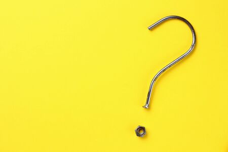 Abstract question mark from a bent nail and nut on a bright yellow background with copy space and...