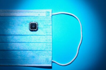 Camera as a symbol of control and surveillance with interference with privacy and medical surgical mask illuminated with vignetting effect, tonedの写真素材