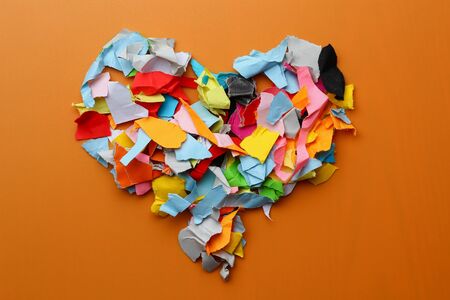Torn colored paper metaphorically depicts a heart on an orange backgroundの写真素材