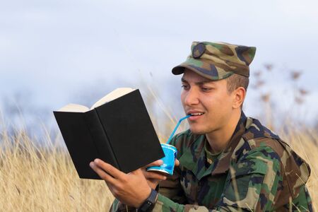 A soldier reads a book and drinks condensed milk from a tin can through a cocktail tubeの写真素材