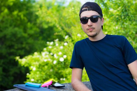 Young freelancer leaned on a concrete curb and resting from work while enjoying natureの写真素材