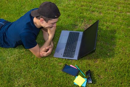 Freelancer works lying on a green lawn with a laptopの写真素材