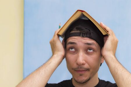 Young guy and a book on his head. Symbol of a house, self-studyの写真素材