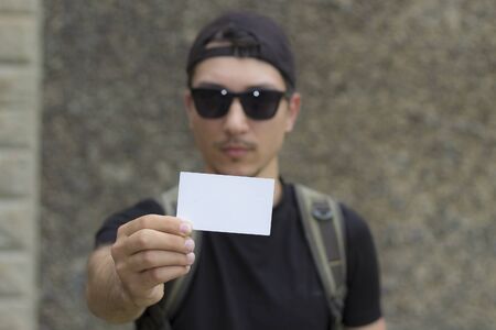 Hand with a white business card and space for text. Blurred tourist with a backpack in the backgroundの写真素材