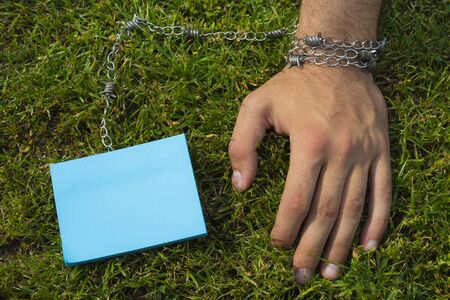 A hand tied to a color sticker with a metal chain, on a background of grass lawn, toned, with copy...