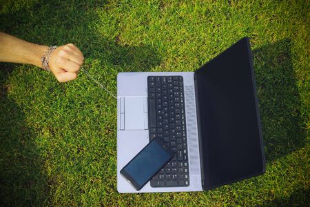 Hand tied to a laptop with a metal chain, toned. The concept of dependence on gadgets, social networks and the Internet, commitment and affection, the trap of freedom of remote work.の写真素材