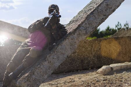 Soldiers airsoft in military clothes is shooting from behind a concrete slab on a background of...
