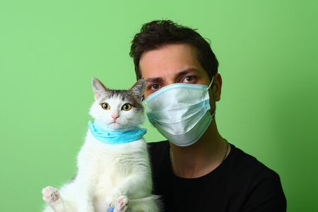 A young man or guy and cat dressed in medical surgical masks on their faces. The concept of love and care for pets during the Covid-19 pandemicの写真素材