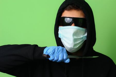 Young male gangster or criminal in a medical surgical mask and sunglasses dressed in black clothes...