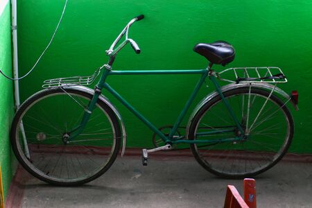 An old classic bike is standing in the stairwell on the background of a green wall under the window.