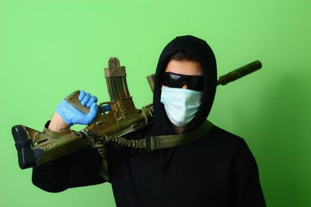 Young male gangster or criminal in a medical surgical mask and sunglasses dressed in black clothes...