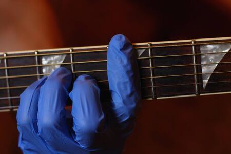 A musician plays with gloves on a musical instrument in an audio studio. The life of a guitarist in the realities of covid-19 pandemicの写真素材